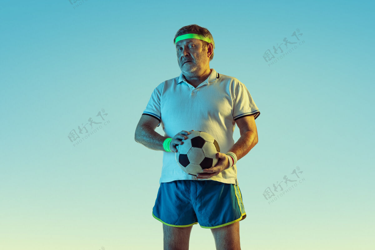 乐趣穿运动服在渐变背景和霓虹灯下踢足球的资深男士休闲高加索健康