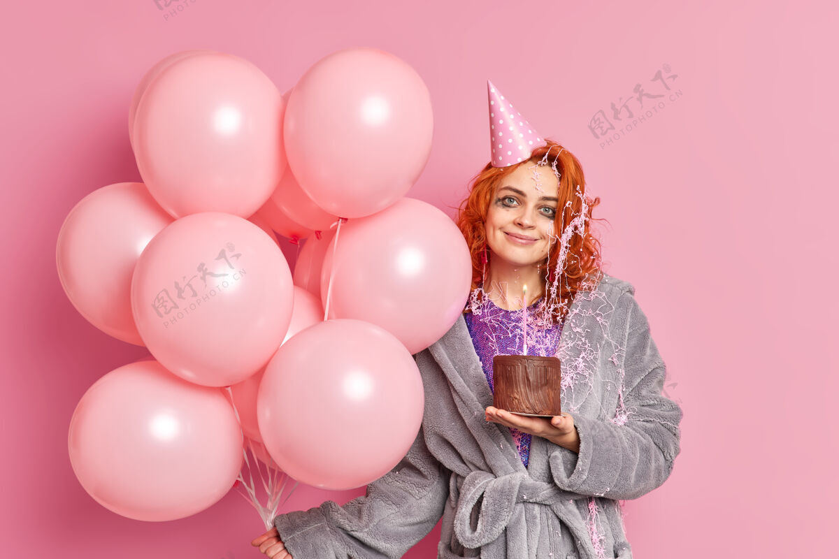 欢乐喜出望外的红发女人捧着巧克力蛋糕庆祝周年快乐派对上穿着休闲服捧着一束粉色充气气球表情欢快微笑活动化妆