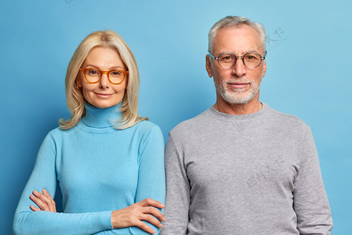 金发成熟女人和男人的肖像 穿着休闲服 站在蓝色的墙上 表情平静 直视前方老年人高领毛衣爱