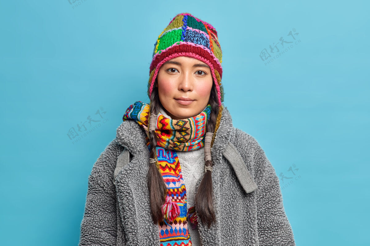 传统严肃的斯堪的纳维亚女人梳着辫子 穿着暖和的冬装 平静地看着前面 在蓝色的墙上摆着姿势青少年请外套