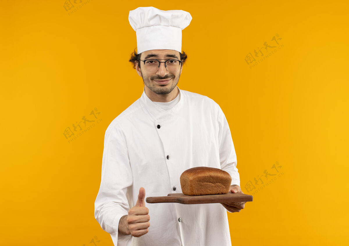 制服年轻的男厨师穿着厨师制服 戴着眼镜 拿着面包 站在黄色的墙板上厨师烹饪眼镜