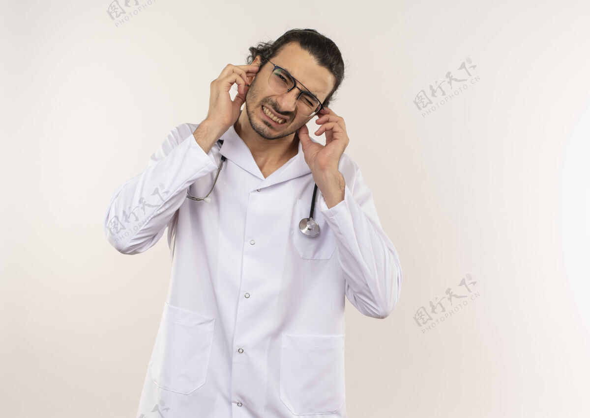 封闭神经质的年轻男医生 戴着眼镜 穿着白色长袍 带听诊器 在隔离的白色墙壁上闭着耳朵 留着复印空间眼镜戴医生