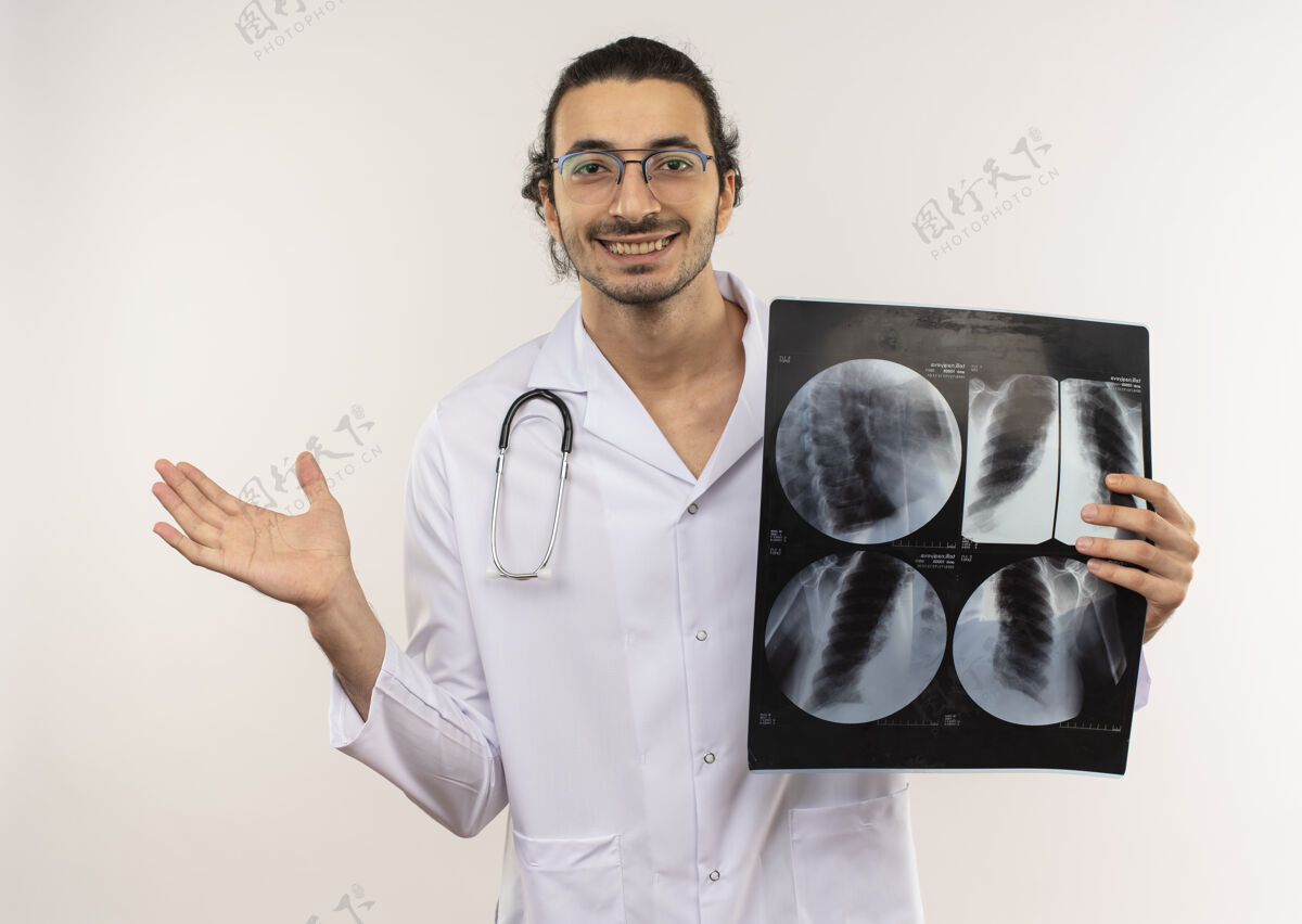 医生面带微笑的年轻男性医生 戴着眼镜 身穿白色长袍 听诊器拿着x光片 用手指着隔离的白色墙壁 并留有复印空间点听诊器持有