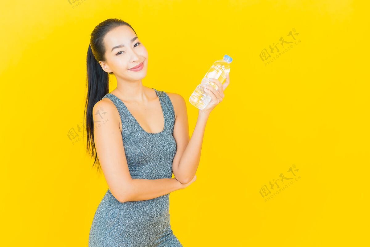 亚洲在黄色的墙上画一幅美丽的亚洲年轻女子 穿着运动服 喝着瓶装水漂亮护理运动