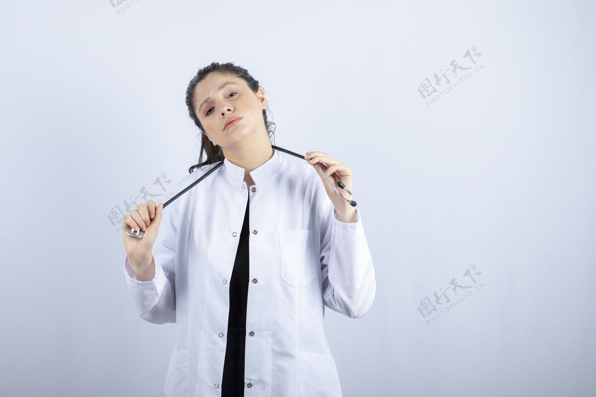 女人穿着白大褂的漂亮女医生在白墙上摆好听诊器的姿势医生工人自信