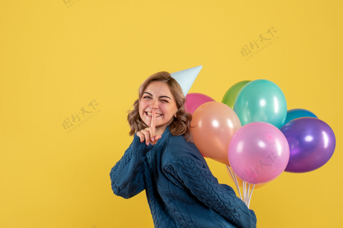 背面年轻的女性把五颜六色的气球藏在黄色的背上年轻女性视图气球
