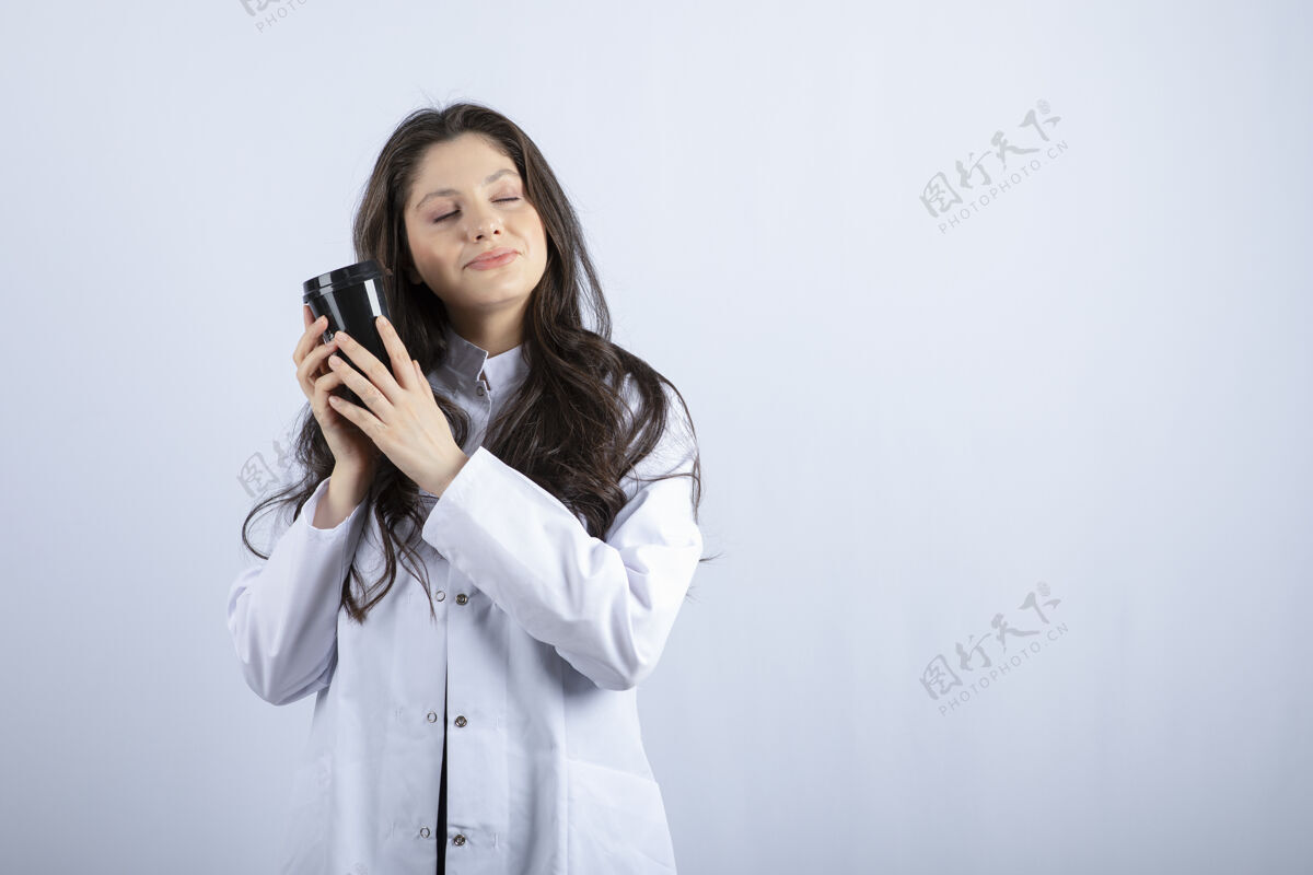 休息一张女医生的画像 她拿着一杯咖啡睡在白墙上工人护理医药