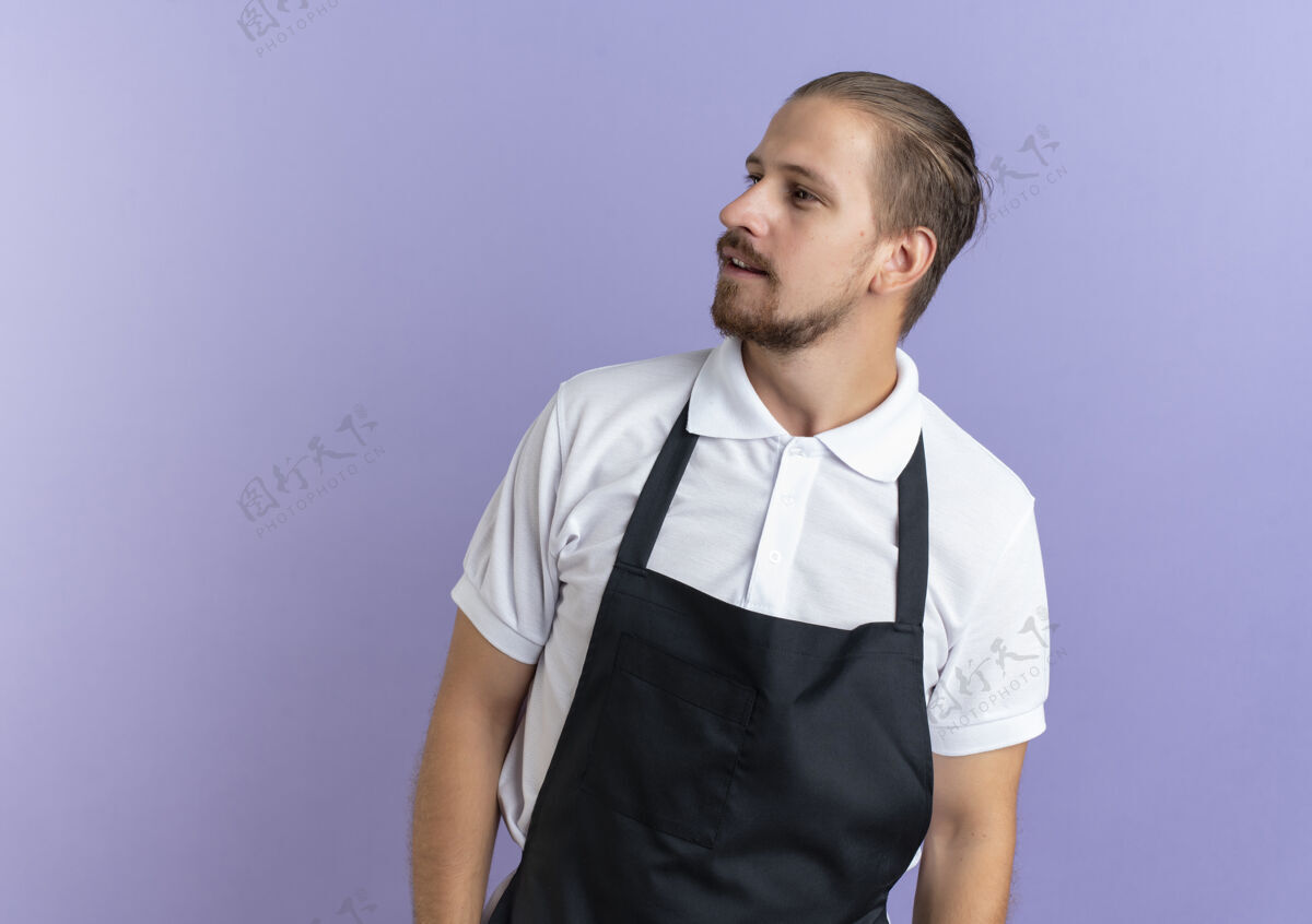 制服印象深刻的年轻英俊的理发师穿着制服站在一边看着孤立的紫色与复制空间穿着印象复制