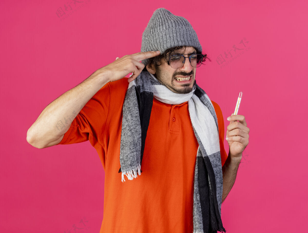 压力紧张的年轻白种人 戴着眼镜 戴着帽子 戴着围巾 拿着温度计 在深红的背景下做着自杀的手势自杀疾病围巾