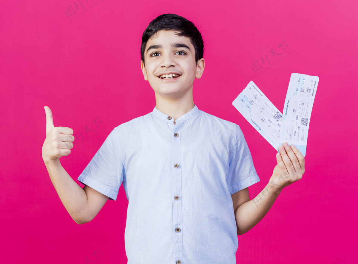 拇指快乐的年轻白人男孩看着直拿着飞机票显示拇指上孤立的深红色背景年轻快乐机票