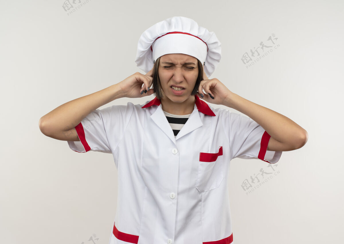 耳朵恼怒的年轻女厨师穿着厨师制服把手指放在耳朵上闭着眼睛孤立在白色女性手指烹饪