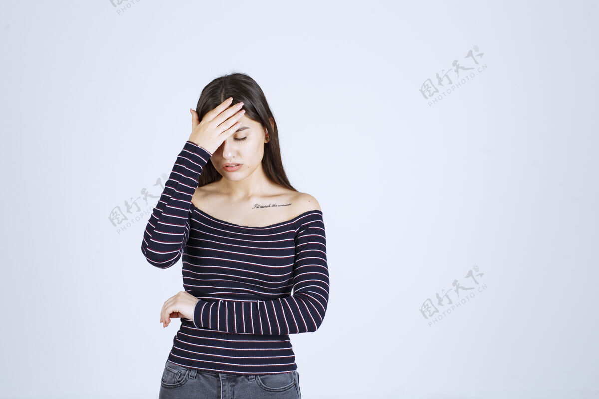 疼痛一个穿着条纹衬衫的年轻女人因为头痛而抱着头成人人害羞