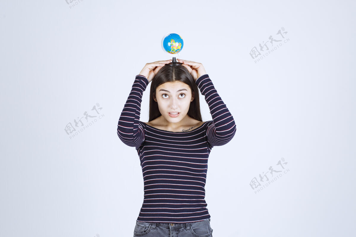 姿势穿着条纹衬衫的年轻女子双手捧着一个迷你地球仪世界人类女性