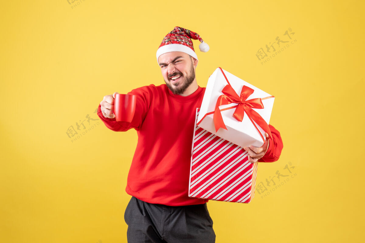 圣诞节前视图年轻男性 圣诞礼物和黄色背景上的一杯茶成人年轻男性背景