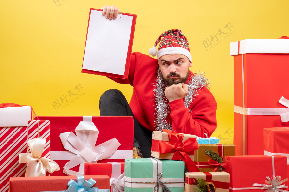 圣诞节正面图：年轻男性围坐在黄色的桌子上 拿着纸条送礼物礼物桌子盒子