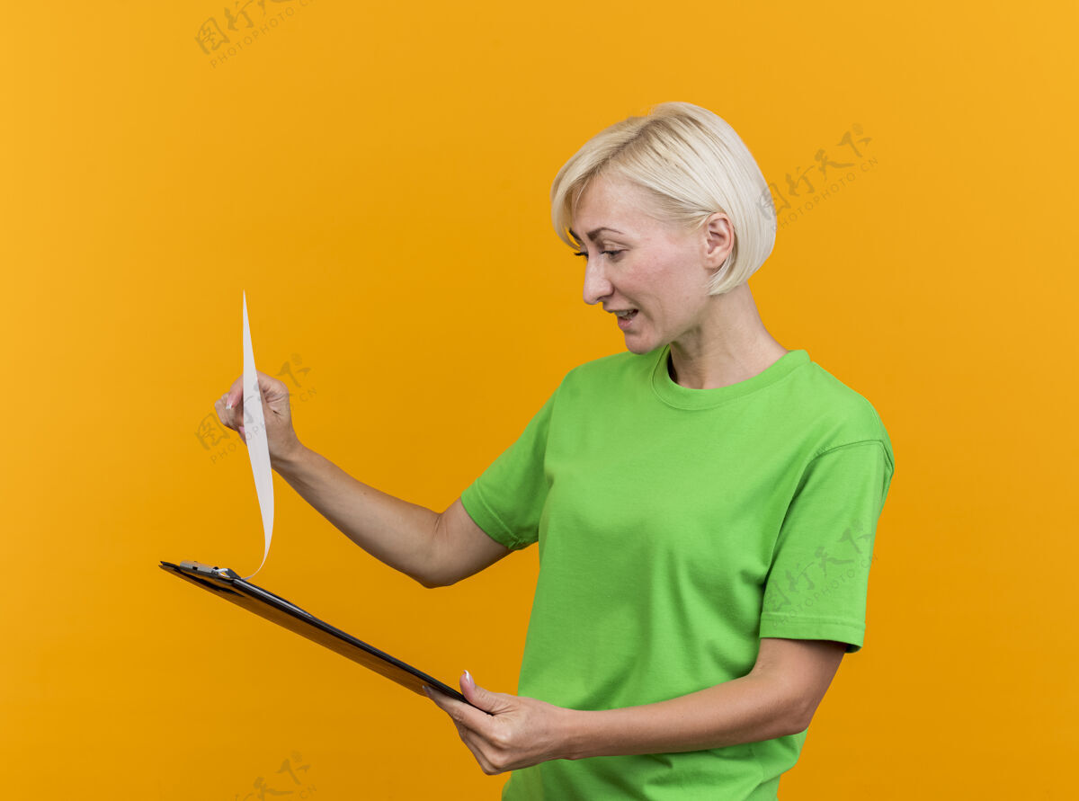 金发高兴的中年金发斯拉夫女人抱着剪贴板看着孤立的黄色背景中年剪贴板拿着