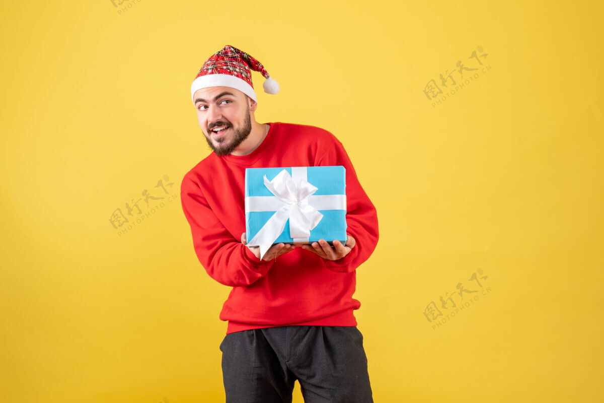 雪黄色背景下手持圣诞礼物的年轻男性正面图礼物成人男性