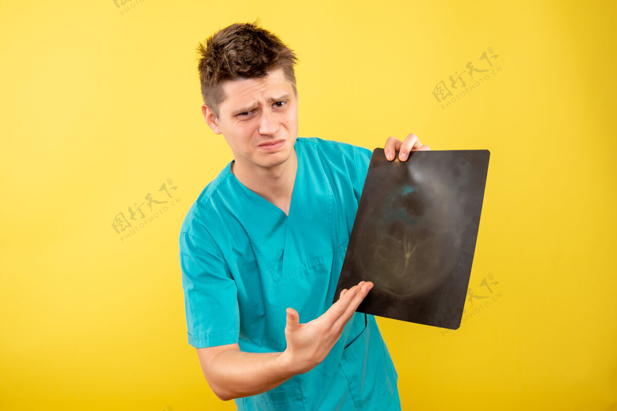 背景正面图身穿医疗服的年轻男医生拿着黄色背景的x光片医学健康套装
