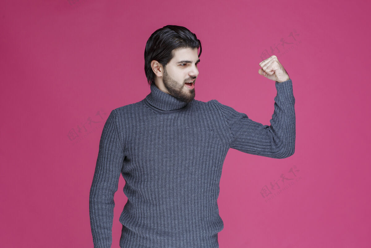 摄影穿灰色毛衣的男人展示他的手臂肌肉成人服装姿势