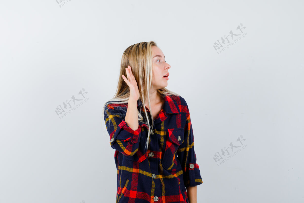 持有穿着格子衬衫的年轻女士手挽着耳朵 面带疑惑地看着前方时尚成人人