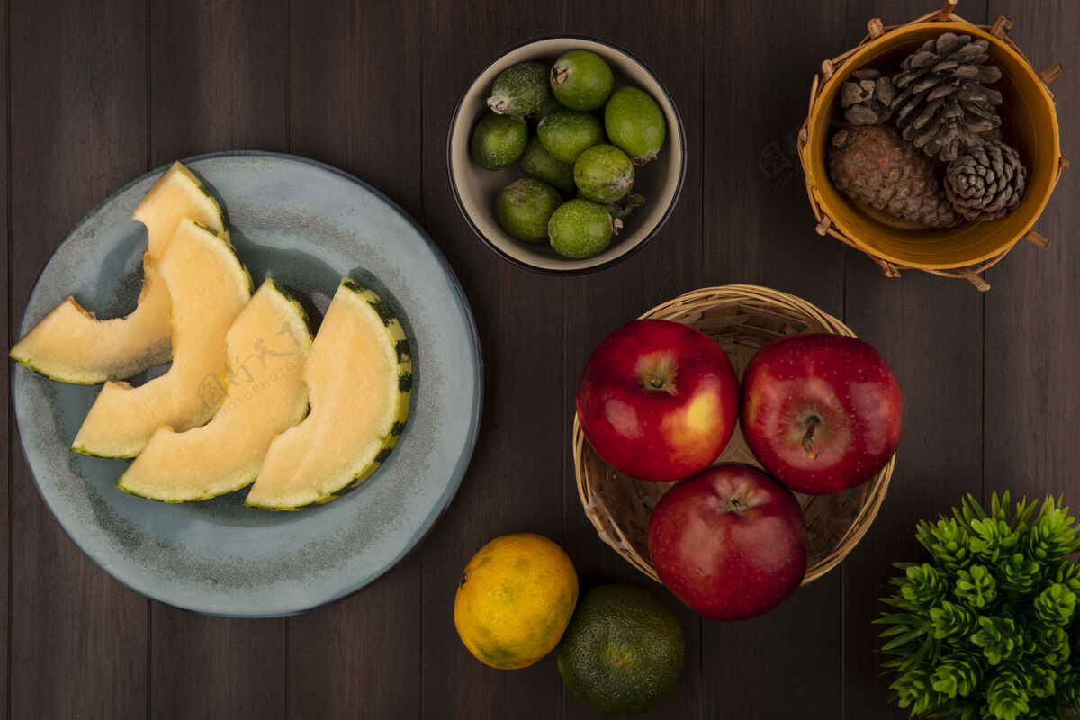 盘子盘子上的哈密瓜片的俯视图 碗上有飞珠 桶上有苹果 木墙上有橘子哈密瓜新鲜火腿