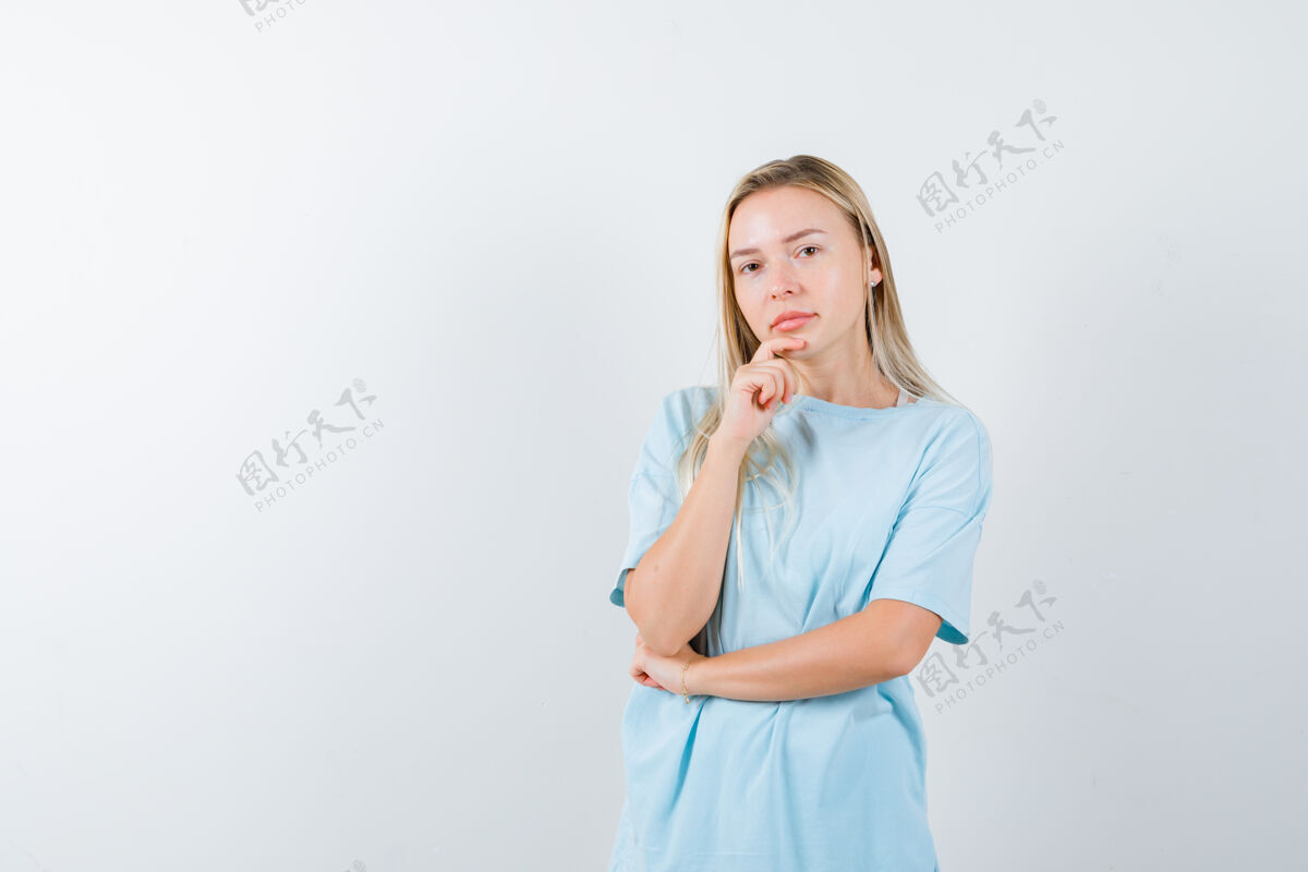 微笑金发女孩用手托着下巴 穿着蓝色t恤 站在思考的姿势里 面带沉思时尚女孩健康