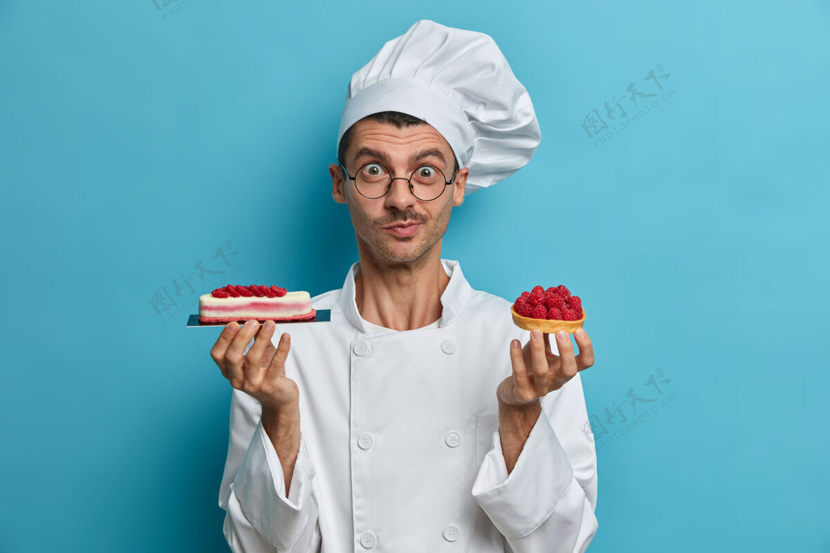 男烹饪 专业 烘焙概念年轻的男性厨师持有美味的糖果 甜点装饰浆果人厨房帽子