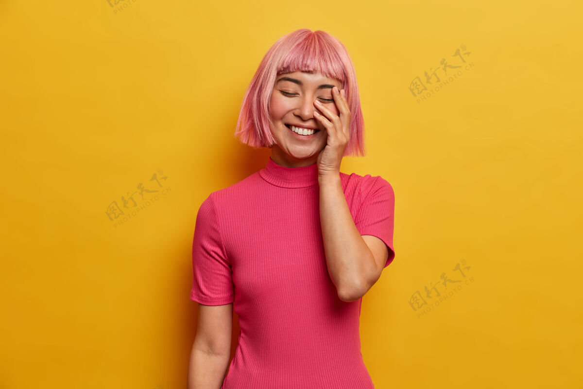 表情年轻的喜洋洋的女人笑得很开心 做脸掌心 笑得合上眼睛 露出白色的牙齿 有粉红色的头发模特年轻成人