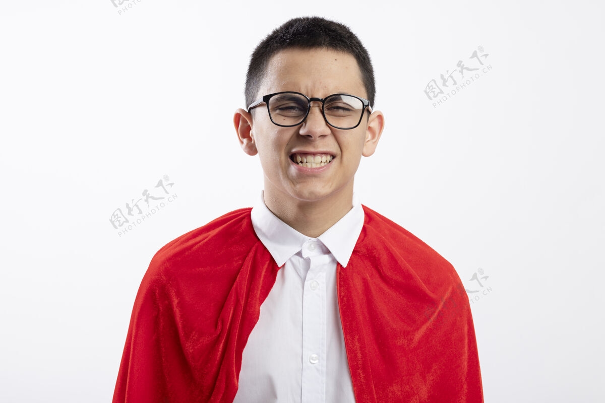 微笑身着红色斗篷 面带微笑的年轻超级英雄男孩戴着眼镜 看着隔离在白色背景上的相机穿着红色年轻
