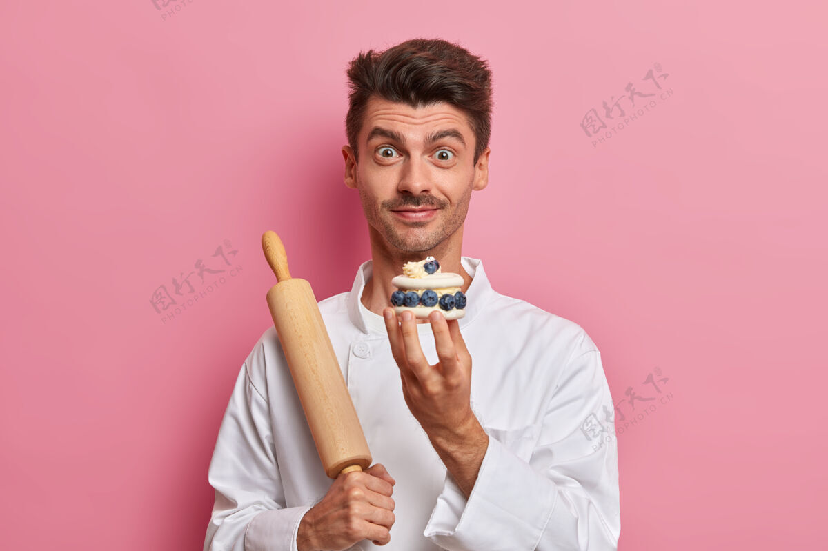 厨房糕点厨师手拿奶油蛋糕 讲述美味糖果的配方 在咖啡馆当厨师 身着白色制服木材制服准备