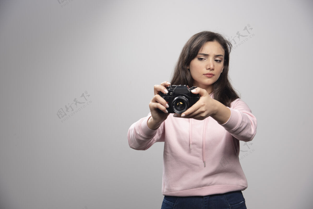 女人漂亮的年轻女子在灰色的墙上用相机拍照人模特漂亮