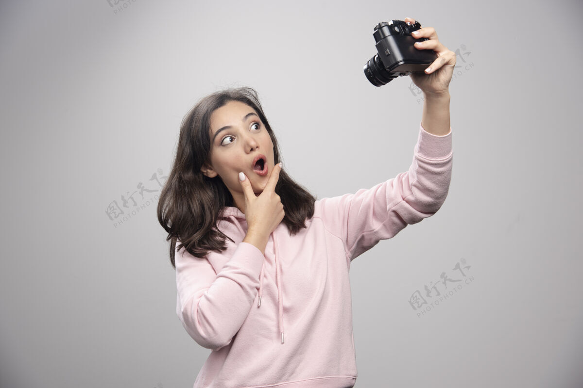 女人漂亮的年轻女子在灰色的墙上用相机自拍墙年轻漂亮