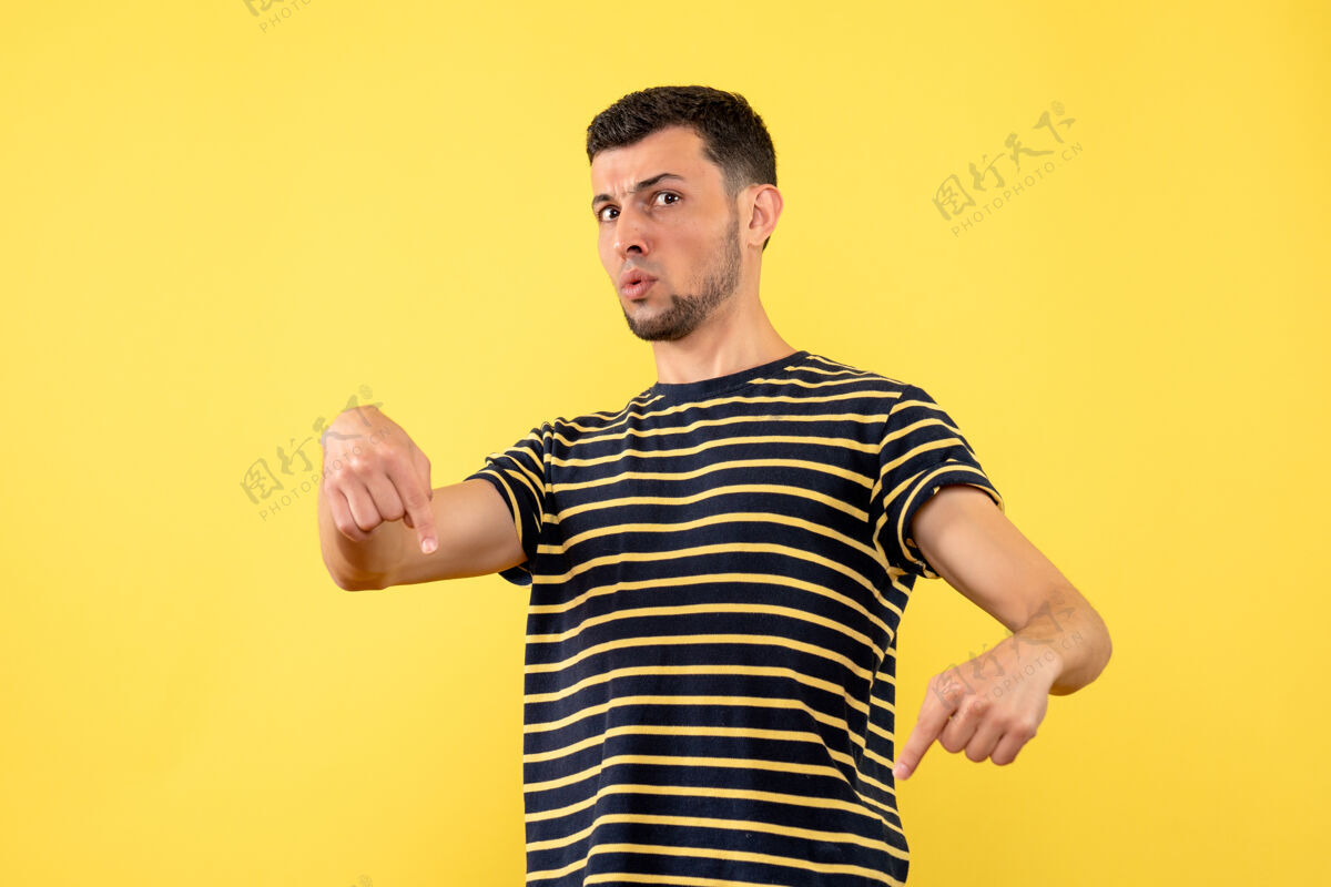 年轻人正面图身穿黑白条纹t恤的年轻人指着地板黄色孤立的背景男T恤黑