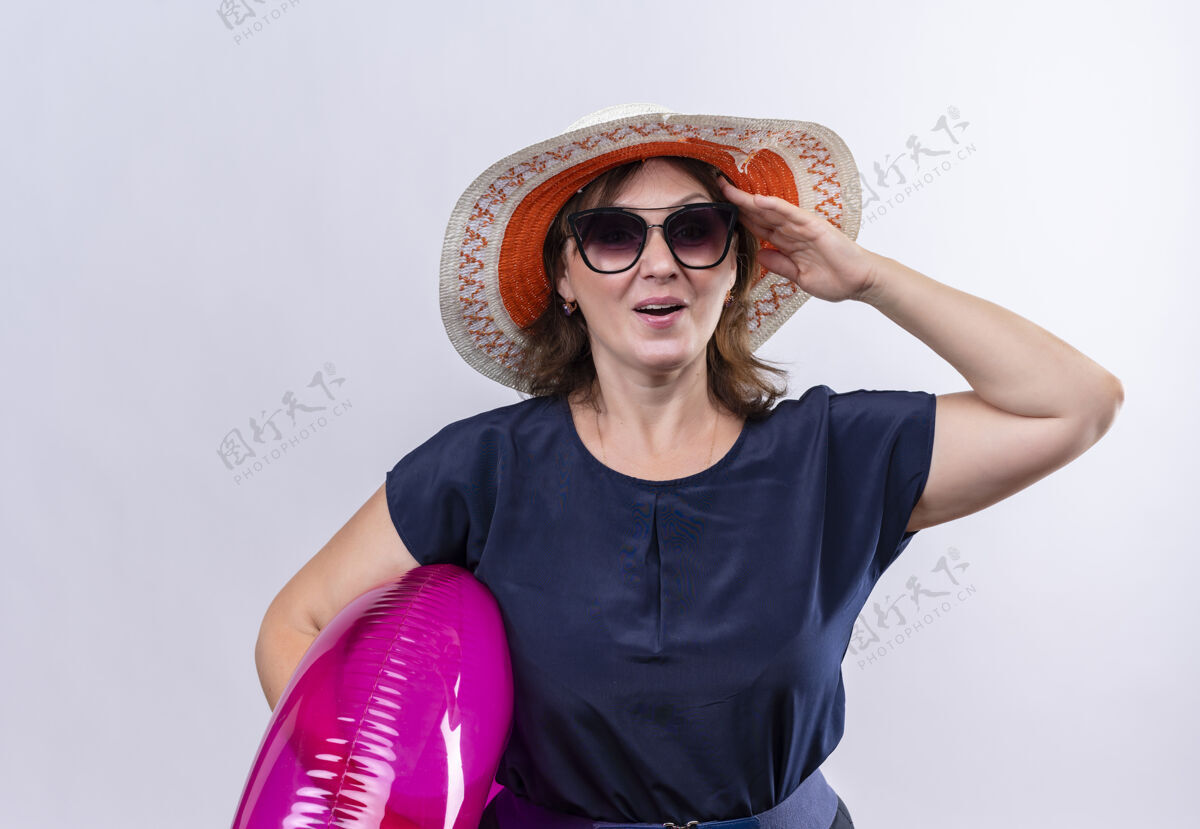 请戴高兴的中年旅行家女子戴着眼镜 戴着帽子 手持充气戒指 孤零零地挂在白色的墙上帽子充气女士