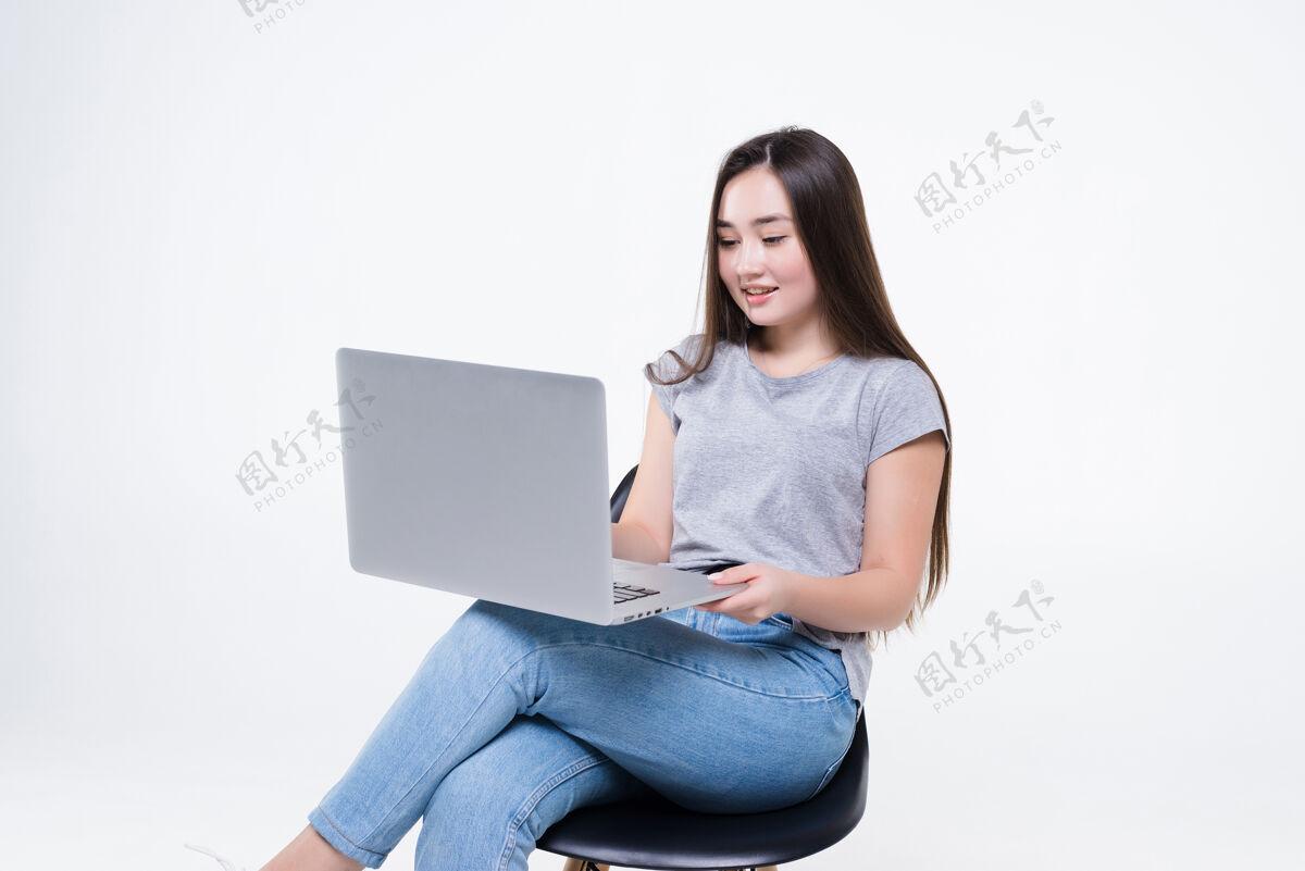 自信亚洲女人坐在椅子上一边打电话一边看笔记本电脑一个工作的女人自信地交叉着双腿坐着坐着自由职业者人