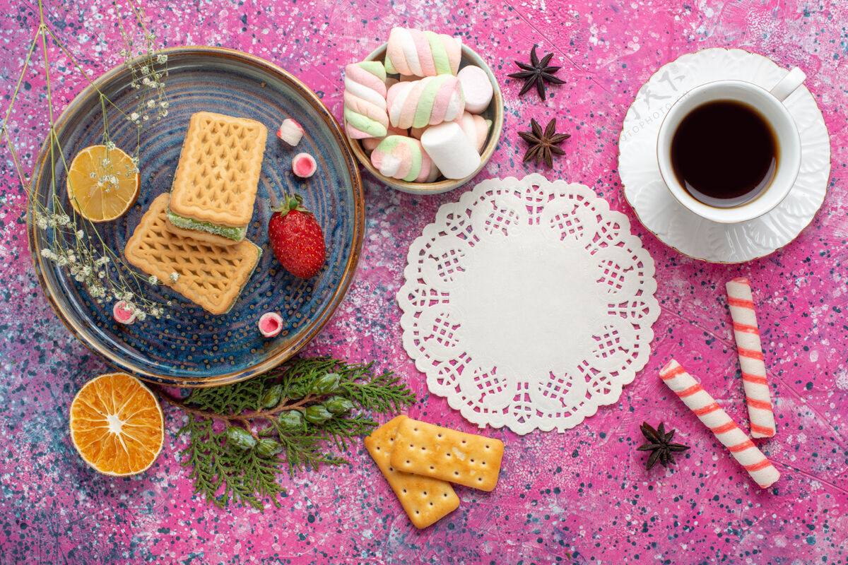 鲜花浅粉色表面上有一杯茶和棉花糖的美味华夫饼俯视图茶顶视图棉花糖