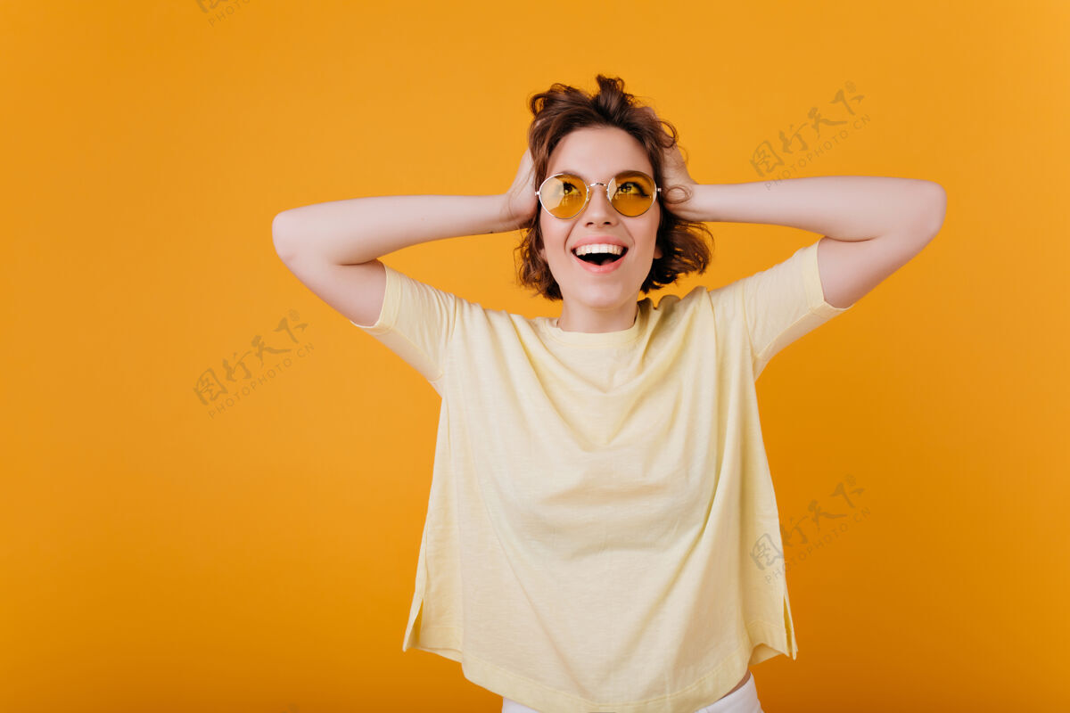 表情穿着超大黄色t恤的兴奋的年轻女士抚摸头部的室内肖像情绪激动的高加索女孩开心地笑着室内肖像微笑