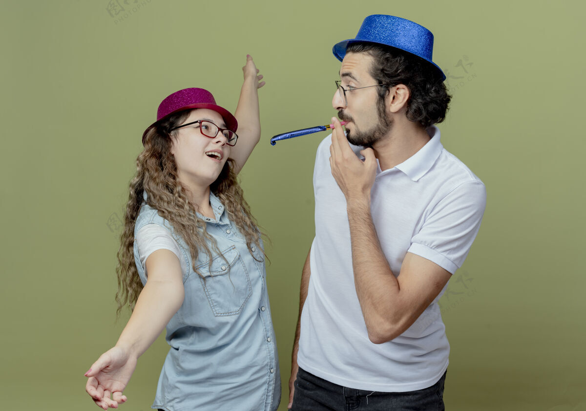绿色一对年轻夫妇戴着粉色和蓝色的帽子看着对方女孩摊开双手 男孩吹着隔离在橄榄绿上的哨子粉色手口哨