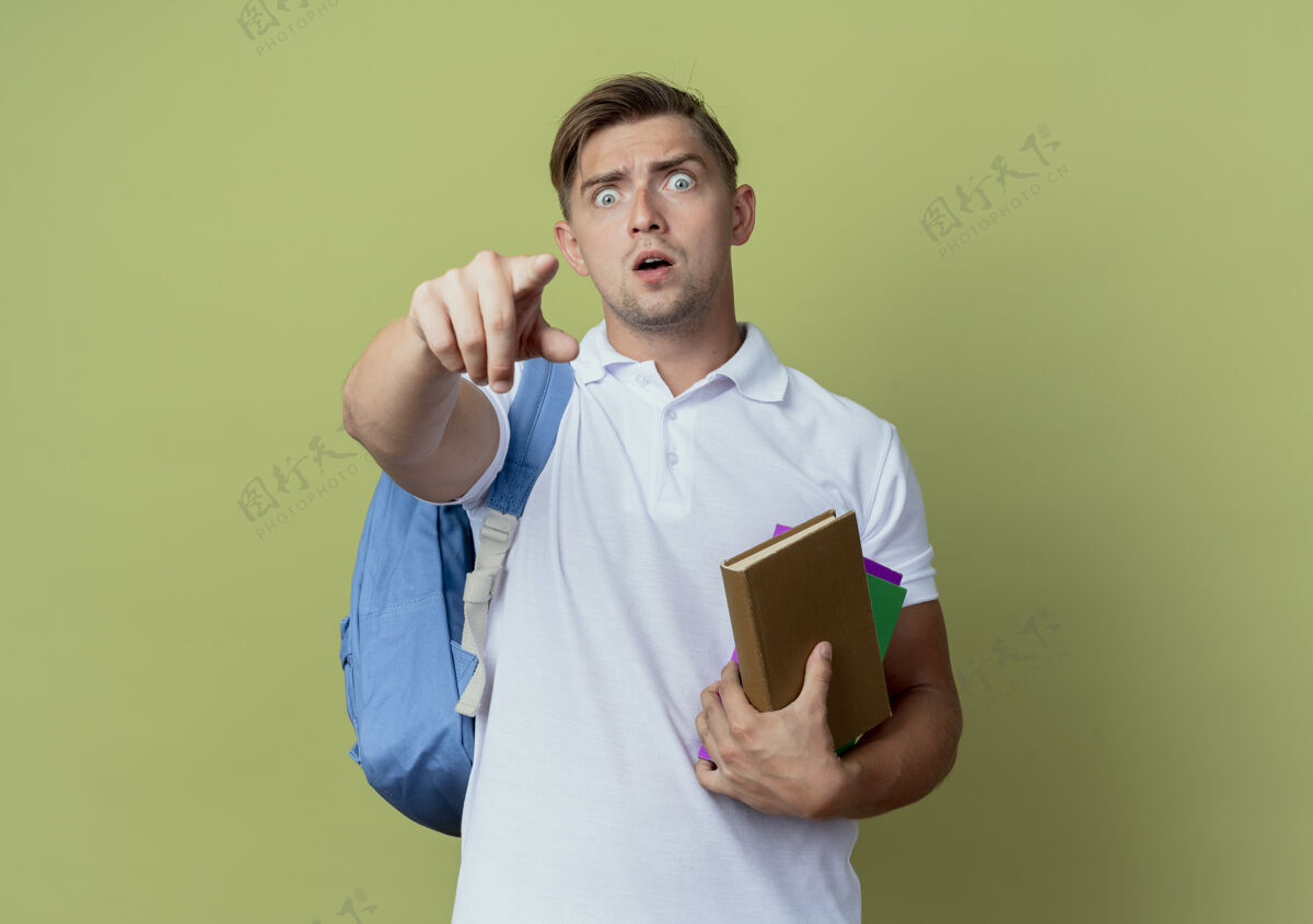 背部惊讶的年轻帅气男学生背着书包拿着书 点着相机隔离在橄榄绿上包年轻点