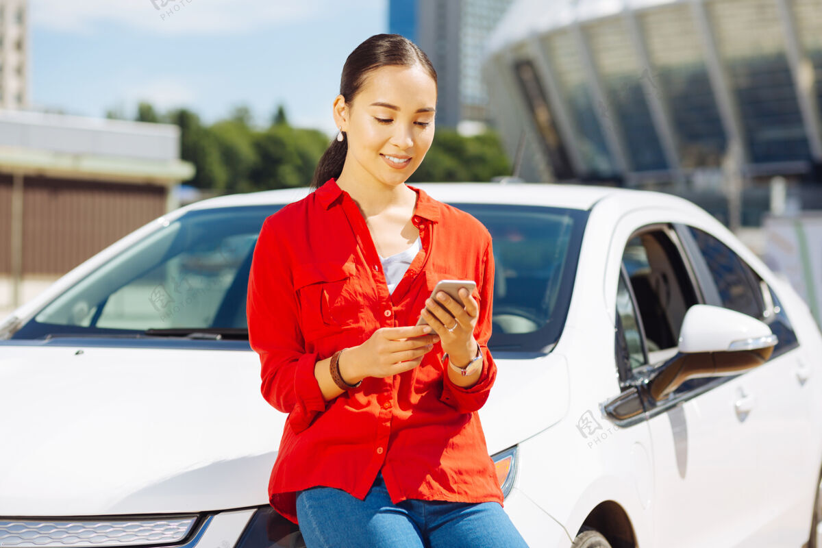街道年轻的女人聪明积极的女人靠在车上看着她的智能手机屏幕永远停车享受