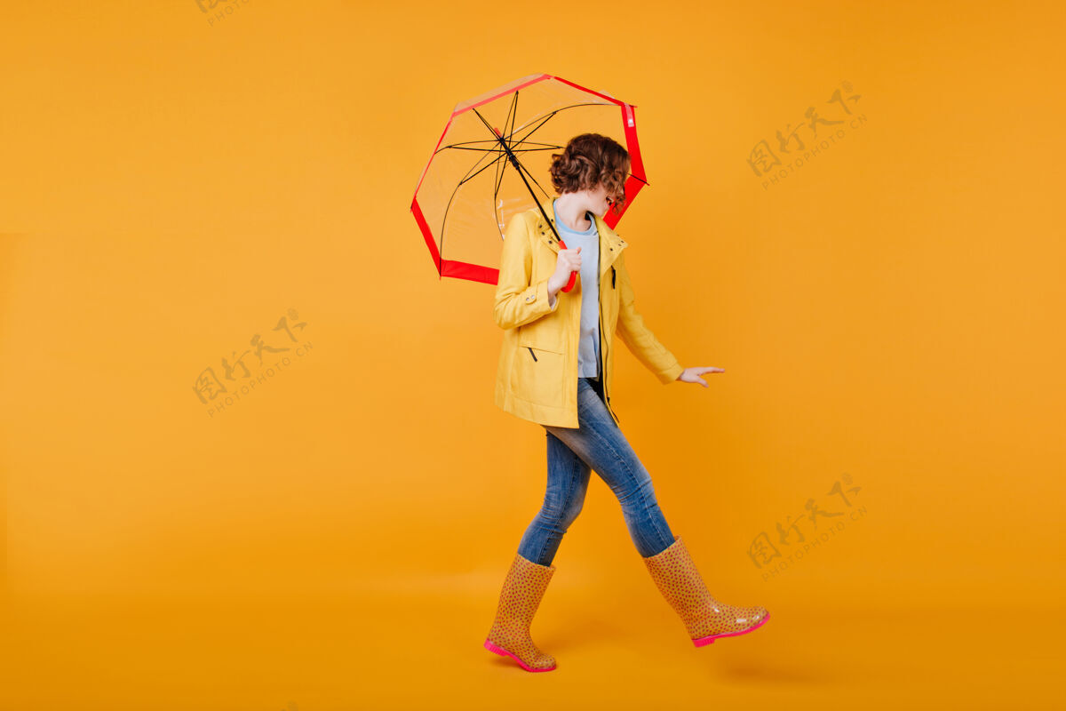 伞穿着滑稽胶鞋的苗条女孩与雨伞共舞的全长肖像卷曲的黑发女士在拍摄秋季服装时玩得很开心舞蹈优雅情绪