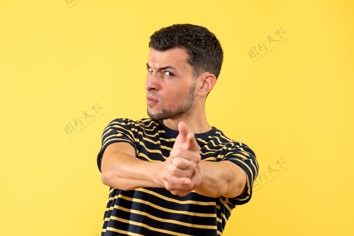 人前视图穿着黑白条纹t恤的年轻人把手指枪放在黄色隔离背景上的相机上枪男视图