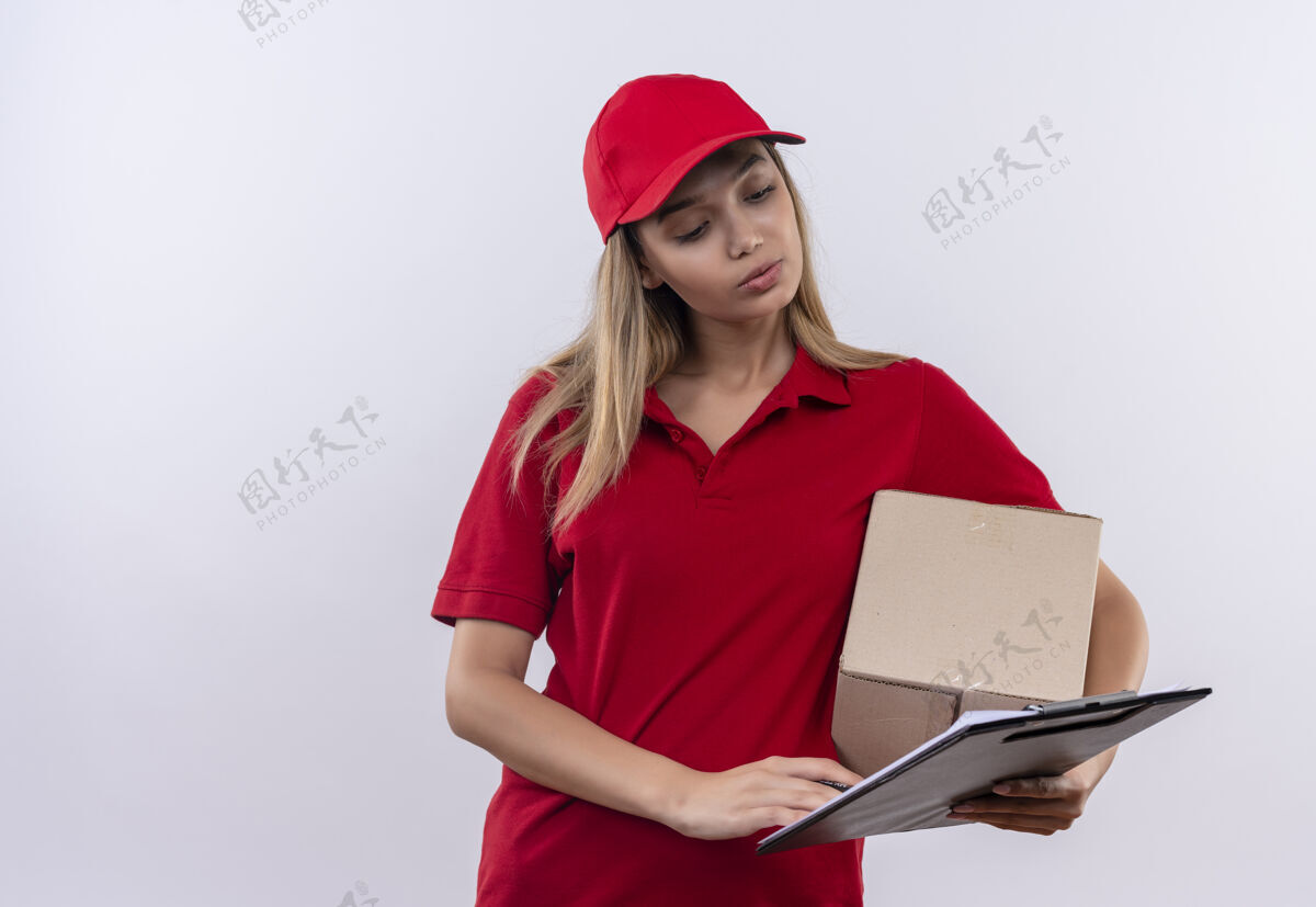 停止想着年轻的送外卖的女孩穿着红色制服 戴着帽子拿着盒子 看着她手里的剪贴板上孤立的白色手势帽子制服