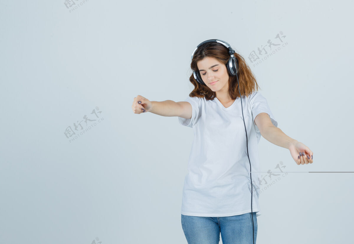 女人穿着白色t恤 牛仔裤 头戴耳机欣赏音乐的年轻女性的肖像 看起来很活泼活泼前面快乐