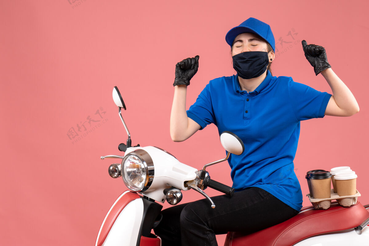 欢乐正面图：戴着口罩的女快递员 送咖啡的人在粉红色上欢呼雀跃女信使流行病摩托车
