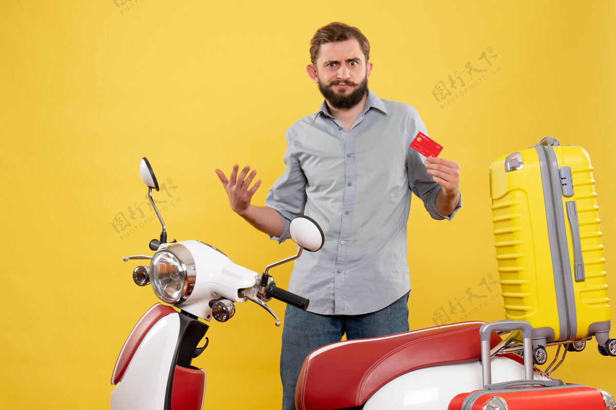 持有旅行概念 雄心勃勃的年轻人站在摩托车后面 拿着黄色的银行卡自行车车辆摩托车
