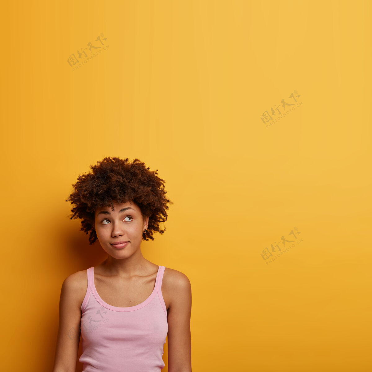 站立沉思卷曲的千禧一代女孩垂直镜头俯瞰 穿着随意 看到一些有趣或诱人的东西 孤立在明黄色的墙上 有沉思的表情女人人美国