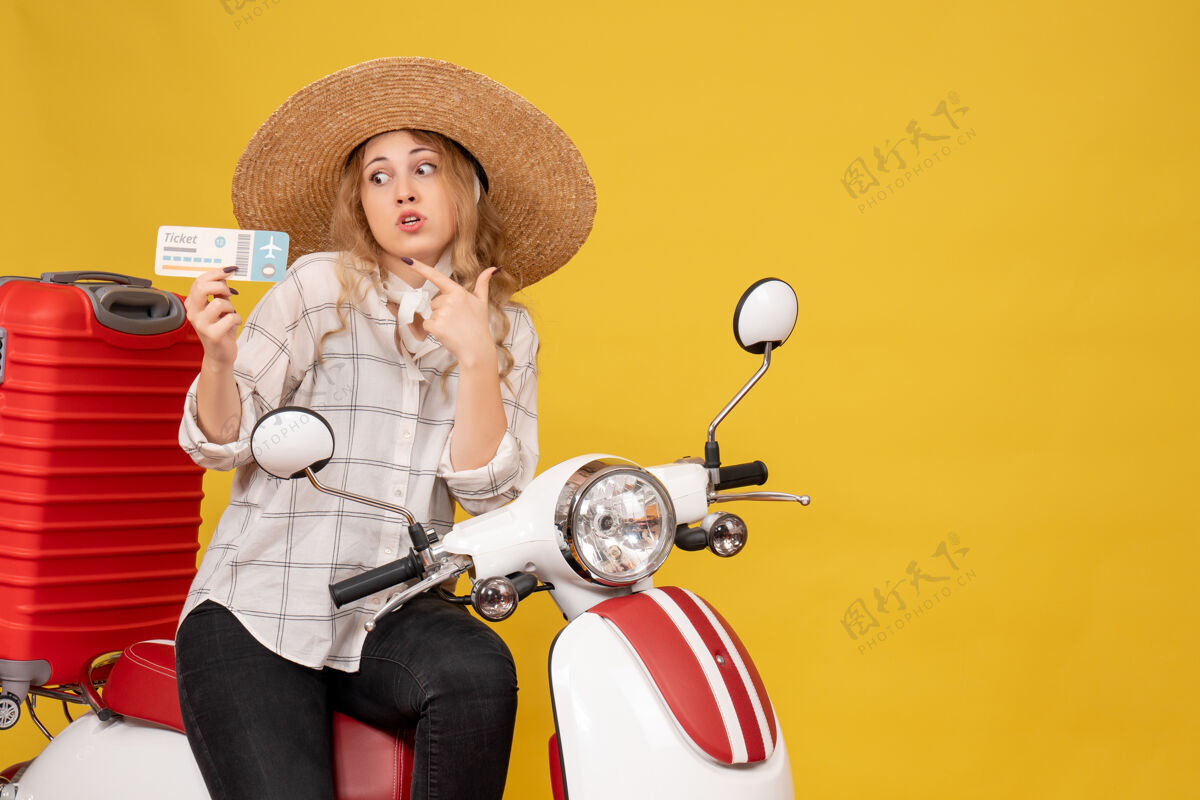 摩托车顶视图震惊的年轻女子戴着帽子 坐在摩托车上 拿着黄色的车票比赛微笑轮廓