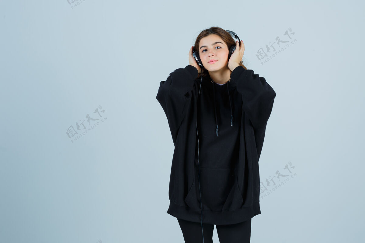 女士年轻女士穿着超大的连帽衫 裤子手拿着耳机 一边听音乐 一边看着正面的风景年轻健康时尚