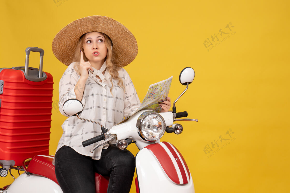 拿着顶视图年轻女子戴着帽子 坐在摩托车上 拿着地图指着黄色年轻女子人向上